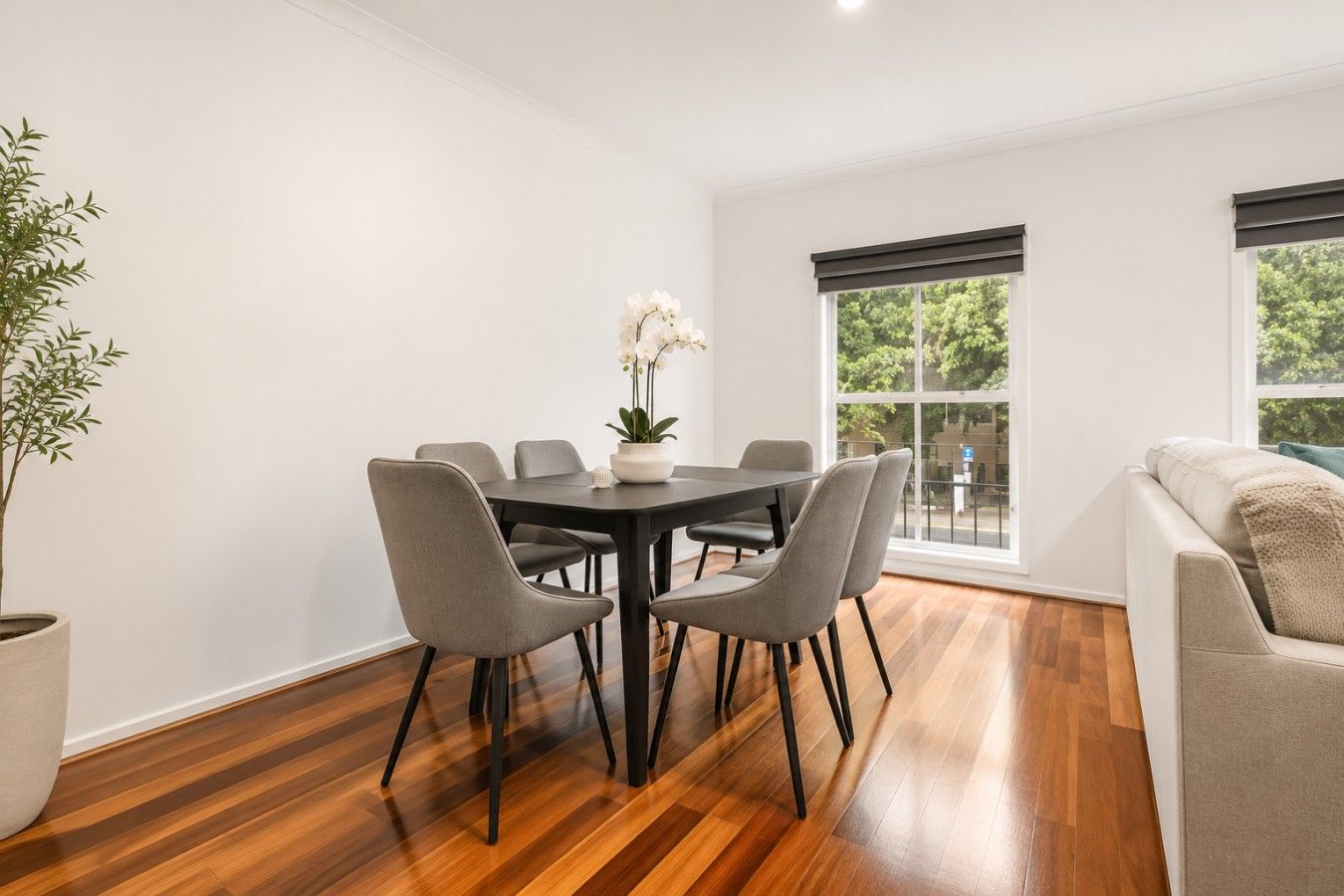 A modern dining area with a round table, six chairs, and a potted plant.