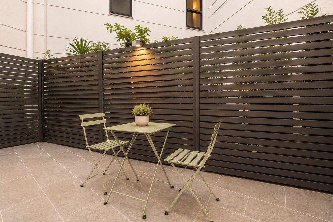 A patio area with a table and chairs, a potted plant, and a dark-colored fence.