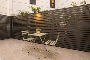 A patio area with a table and chairs, a potted plant, and a dark-colored fence. - Leafy Family 2 Bedroom (South Melbourne)