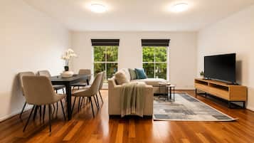 A modern living room with a dining area, a sofa, a TV, and large windows.