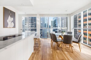 A modern kitchen with a marble countertop, wooden flooring, and a dining area with a table and chairs. - City 4 Bedroom Penthouse (Melbourne)