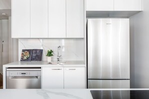 Eine moderne Küche mit weißen Schränken, einem Geschirrspüler aus Edelstahl und einem Kühlschrank von Samsung.