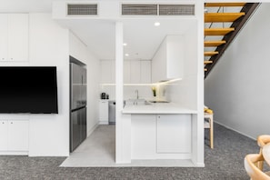 A modern kitchen with white cabinetry, a built-in stove, and a large flat-screen TV. - City Apartment Sleeps 12 (Melbourne)