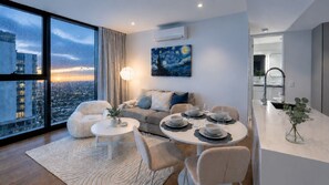 A modern living room with a sofa, two round tables, and a city view through large windows. - Modern City 2 Bedroom Retreat (Melbourne)
