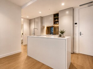 A modern kitchen with a central island, built-in appliances, and a minimalist design. - Modern City 2 Bedroom Retreat (Melbourne)