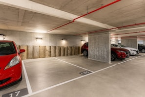 A multi-level underground parking garage with concrete pillars, marked parking spaces, and overhead red pipes. - Bay View 2 Bedroom Apartment (Port Melbourne)