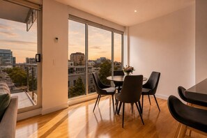 A modern dining area with a city view, large windows, and a round table with chairs. - Bay View 2 Bedroom Apartment (Port Melbourne)