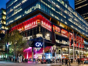 En byggnad med flera våningar, med en tydlig skylt med texten ”DOMAINE”, en logotyp med bokstäverna ”QV” och ett område för fotgängare med träd och liv och rörelse på gatan.