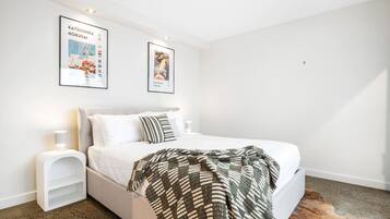 A bedroom with a bed, a nightstand, two framed posters, and a rug.