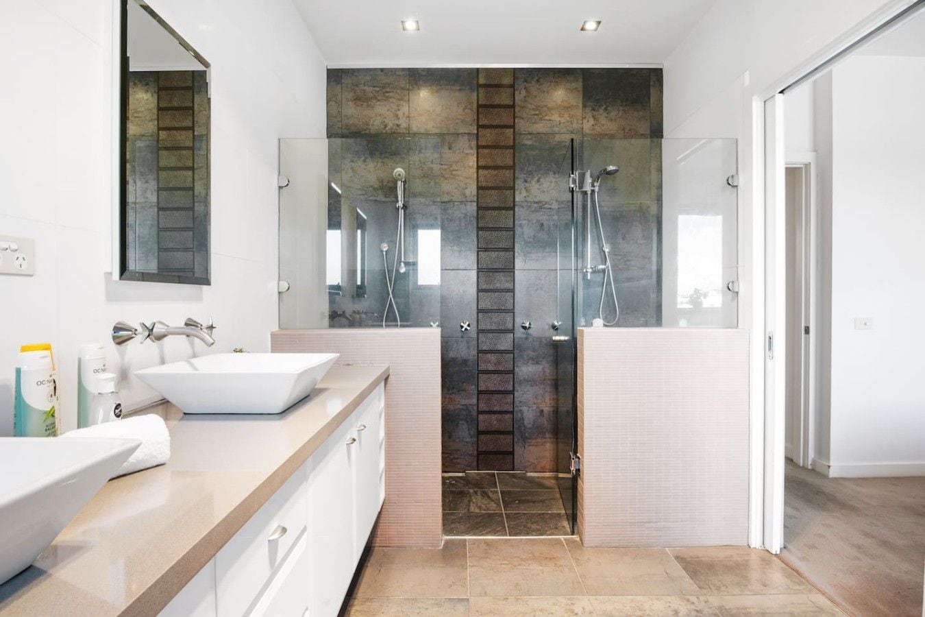 A modern bathroom with two sinks, a glass shower enclosure, and a large mirror.