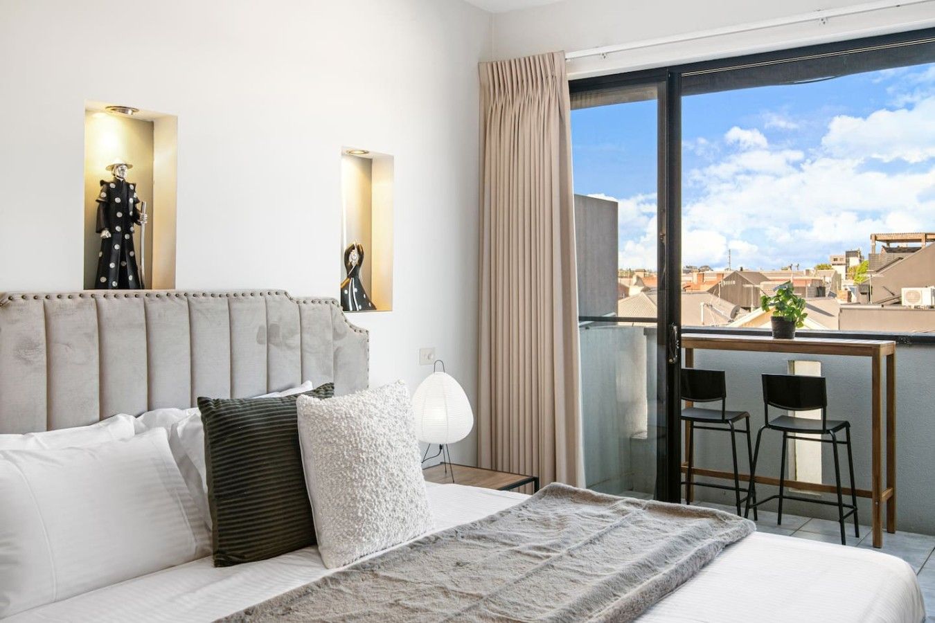 A hotel room with a large bed, a view of the city, and a balcony with chairs.