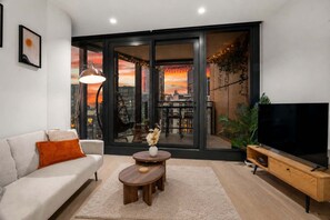 A modern living room with a sofa, a coffee table, a TV, and a large window with a city view. - Skyline Sunset 2 Bedroom (Southbank)