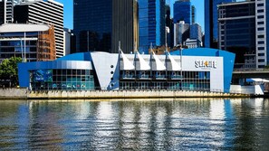 A modern building with a blue and white color scheme, located near a body of water with reflections. - Skyline Sunset 2 Bedroom (Southbank)