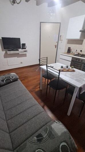 Un espace de vie compact comprenant un canapé, une table à manger avec des chaises, un téléviseur et un coin cuisine.