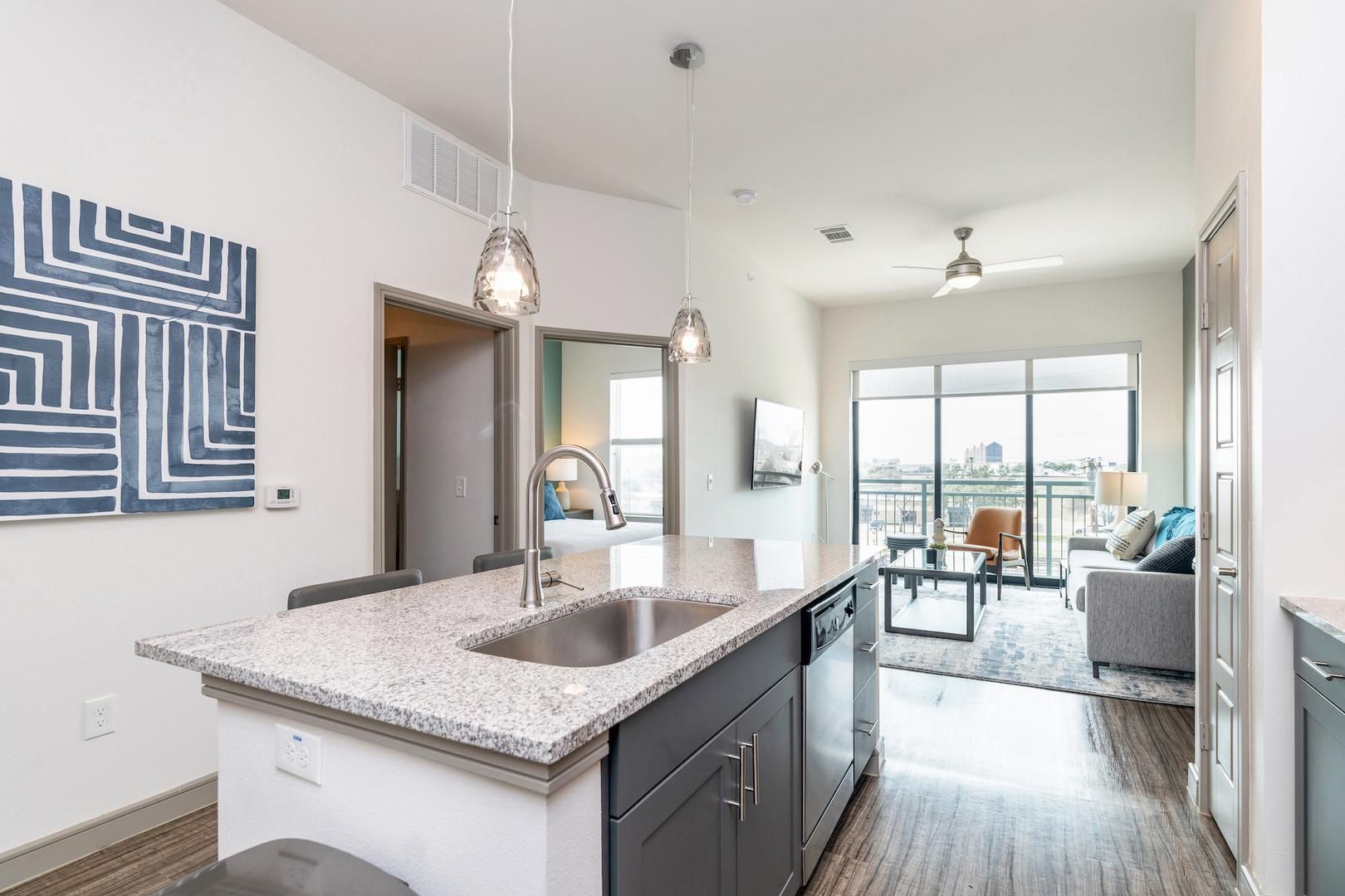 A modern kitchen with granite countertops, a stainless steel sink, and pendant lighting.