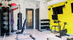 Ein Fitnessstudio mit Trainingsgeräten, einem Boxsack, Hanteln und einem Fahrradergometer.