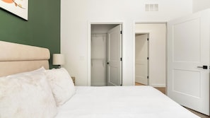 A bedroom with a bed, a nightstand, a lamp, a closet, and a door. - Landing | Incredible 2BD in North Kissimmee (Kissimmee)