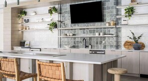 A modern kitchen with a large island, white cabinetry, and a flat-screen TV mounted above the backsplash. - Landing | Incredible 2BD in North Kissimmee (Kissimmee)