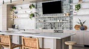A modern kitchen with a large island, white cabinetry, and a flat-screen TV mounted above the backsplash. - Landing | Beautiful 2BD in North Kissimmee (Kissimmee)