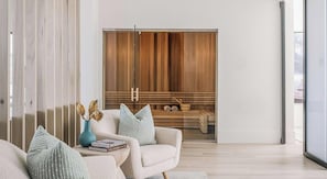 A modern living room with a sofa, pillows, a vase with dried flowers, and a wooden cabinet with a bench. - Landing | Beautiful 2BD in North Kissimmee (Kissimmee)