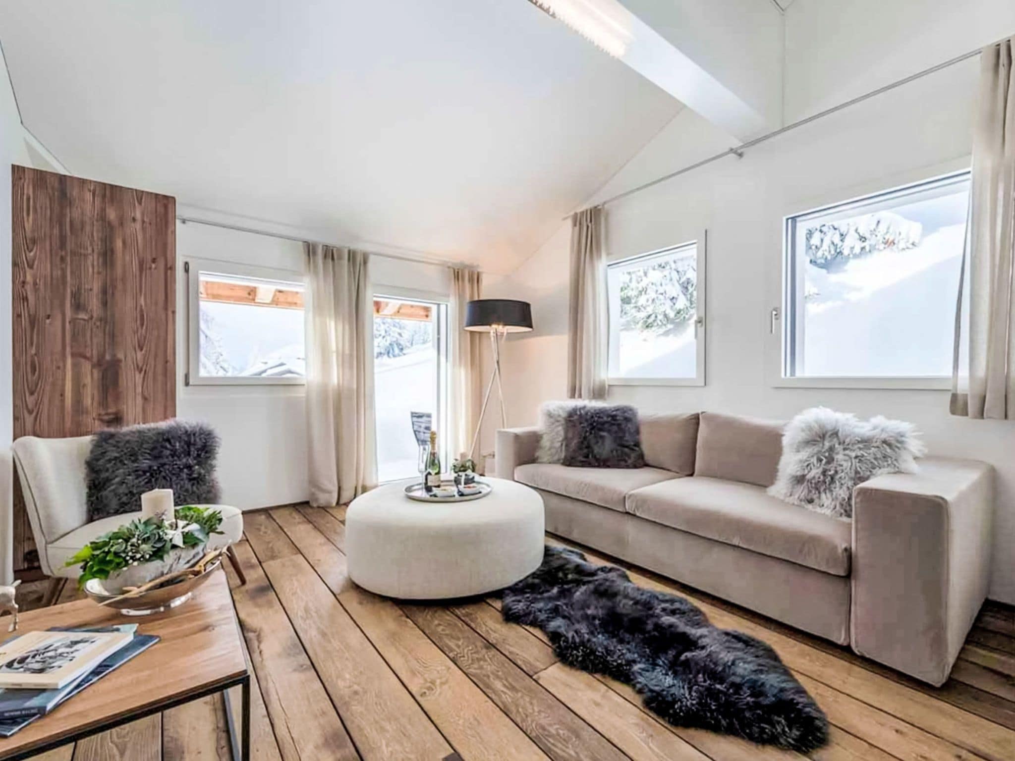 Un salon moderne avec un plancher en bois, un pouf rond, un canapé et une table basse.