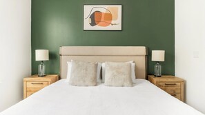 Un lit avec une tête de lit, deux tables de chevet avec des lampes et un tableau abstrait accroché au mur.