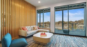 A modern living room with a sectional sofa, a coffee table, and large windows offering a view of the outdoors. - Landing | Chic 1BD, Clubhouse, Gym (Durham)