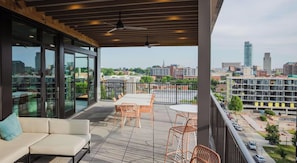 Un balcon aménagé avec un canapé, des chaises et une table, d’où l’on peut admirer une vue sur la ville, avec ses bâtiments et sa rivière.
