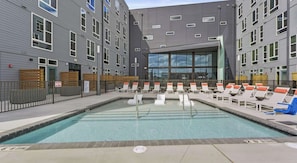 A pool area with lounge chairs and a building with multiple windows. - Landing | Stylish Studio, Clubhouse, Gym (Durham)