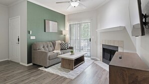 A living room with a sofa, coffee table, fireplace, and a view through a window. - Landing | Beautiful 1BD, Courtyard, Gym (Allen)