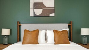 Una habitación de hotel con una cama, dos lámparas de noche, una obra de arte en la pared y una pared verde.