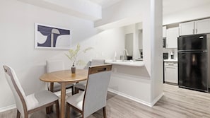 Une cuisine moderne avec des meubles blancs, un réfrigérateur noir et un coin repas comprenant une table en bois et des chaises grises.
