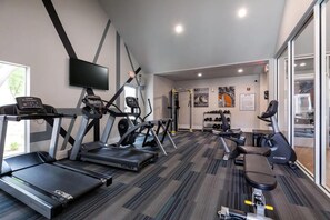 Ein Fitnessraum mit Laufbändern, Crosstrainern und einer Hantelbank.
