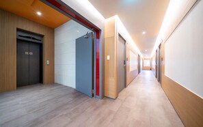 A modern hallway with a wooden floor, a blue door, and a red accent wall.