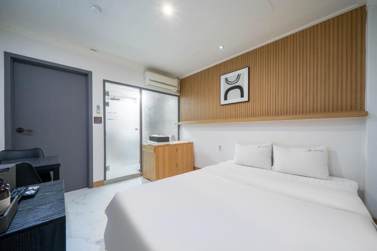 Habitación de hotel con cama, escritorio, silla, armario y baño con ducha.