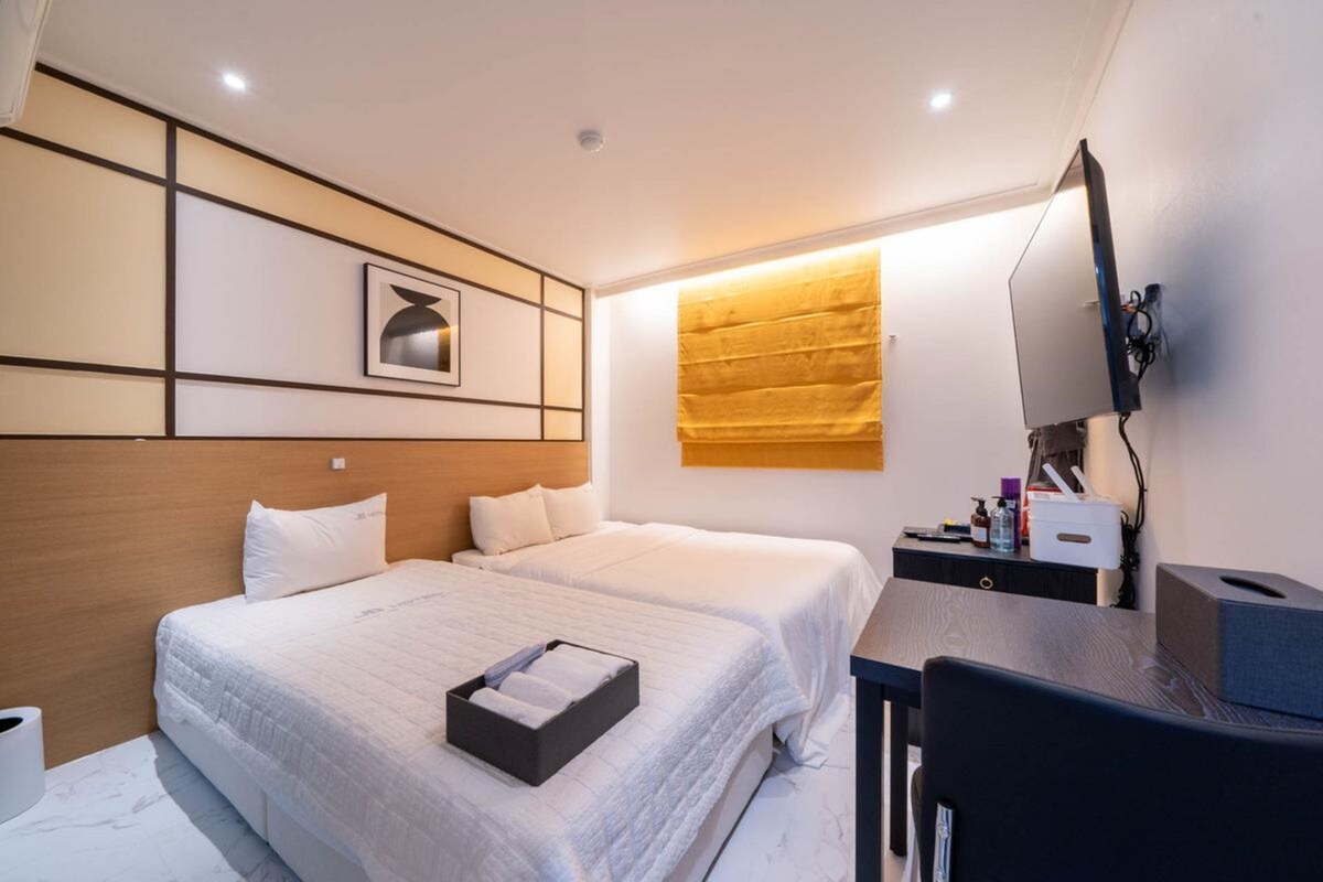 Habitación de hotel con dos camas, un escritorio, una silla, un televisor y una lámpara fijada en la pared.