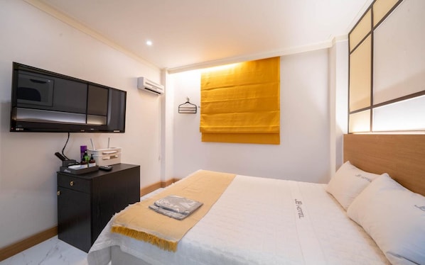 A hotel room with a bed, a bedside table, a TV, and a wall-mounted air conditioning unit.