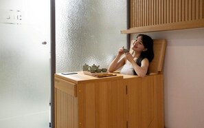 Una persona sentada en una silla de madera con un juego de té sobre una mesa.