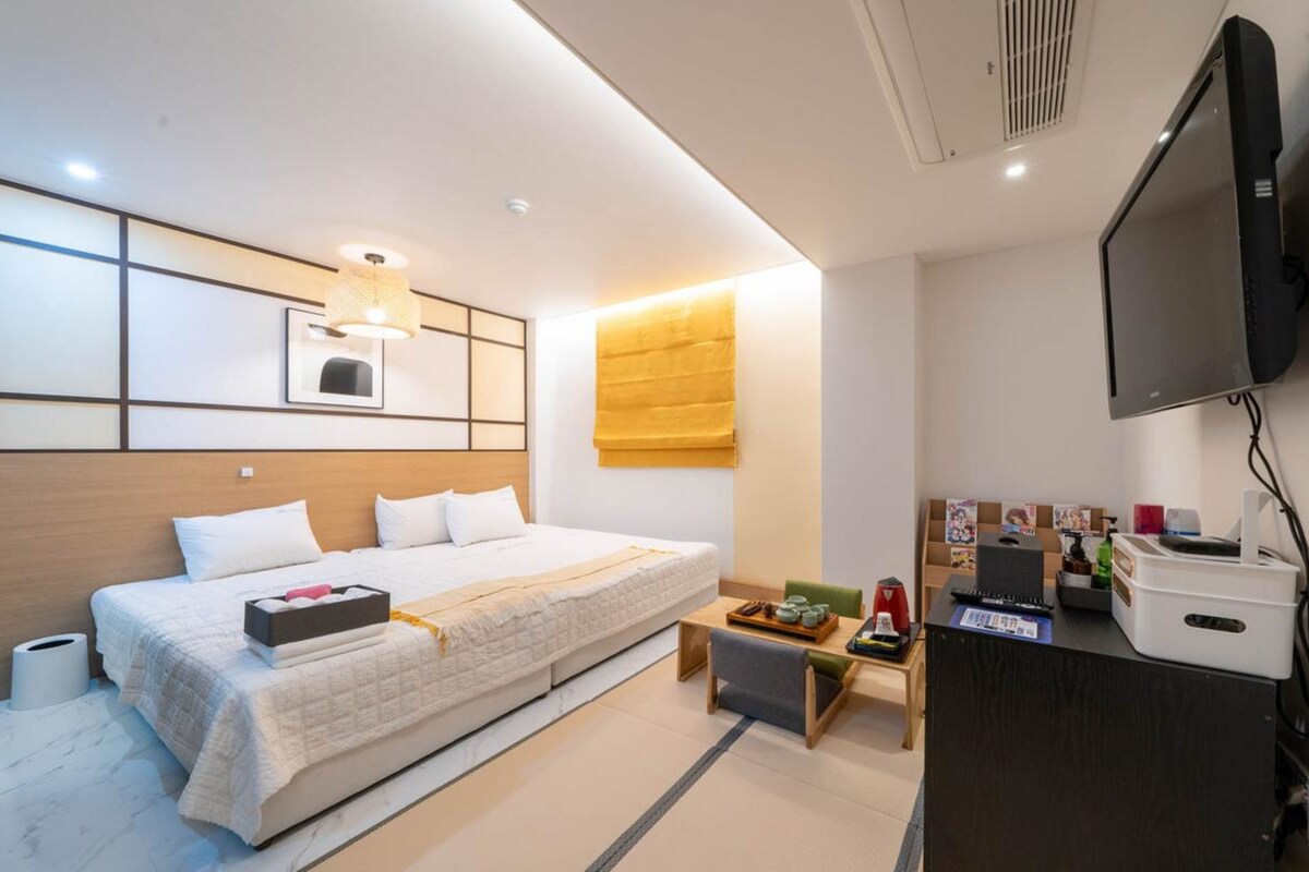 Una habitación de hotel con cama, mesita de noche y televisor montado en la pared.