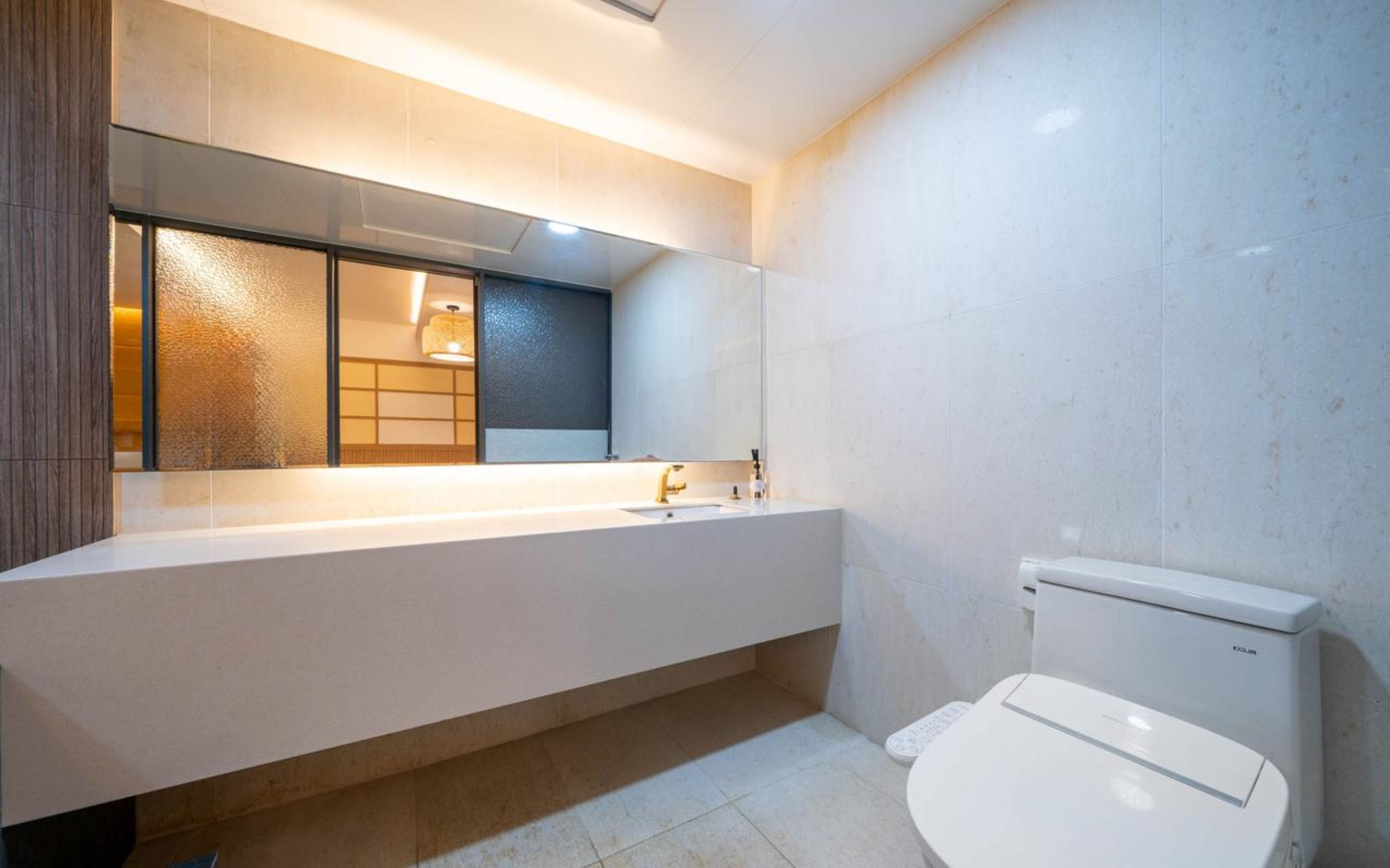 A modern bathroom with a long vanity, a mirror, a toilet, and a shower area.