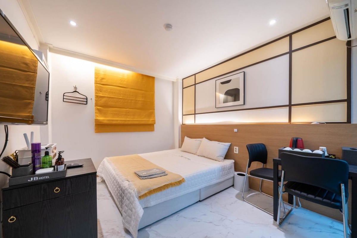 Habitació d'hotel amb un llit, una taula de nit, una cadira, un escriptori i una televisió.