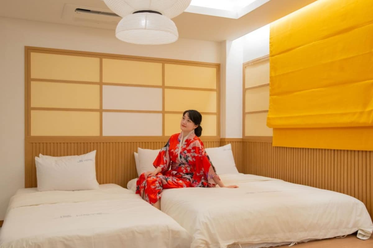 Habitació d'hotel amb dos llits, una finestra gran i vistes, i un ventilador de sostre.