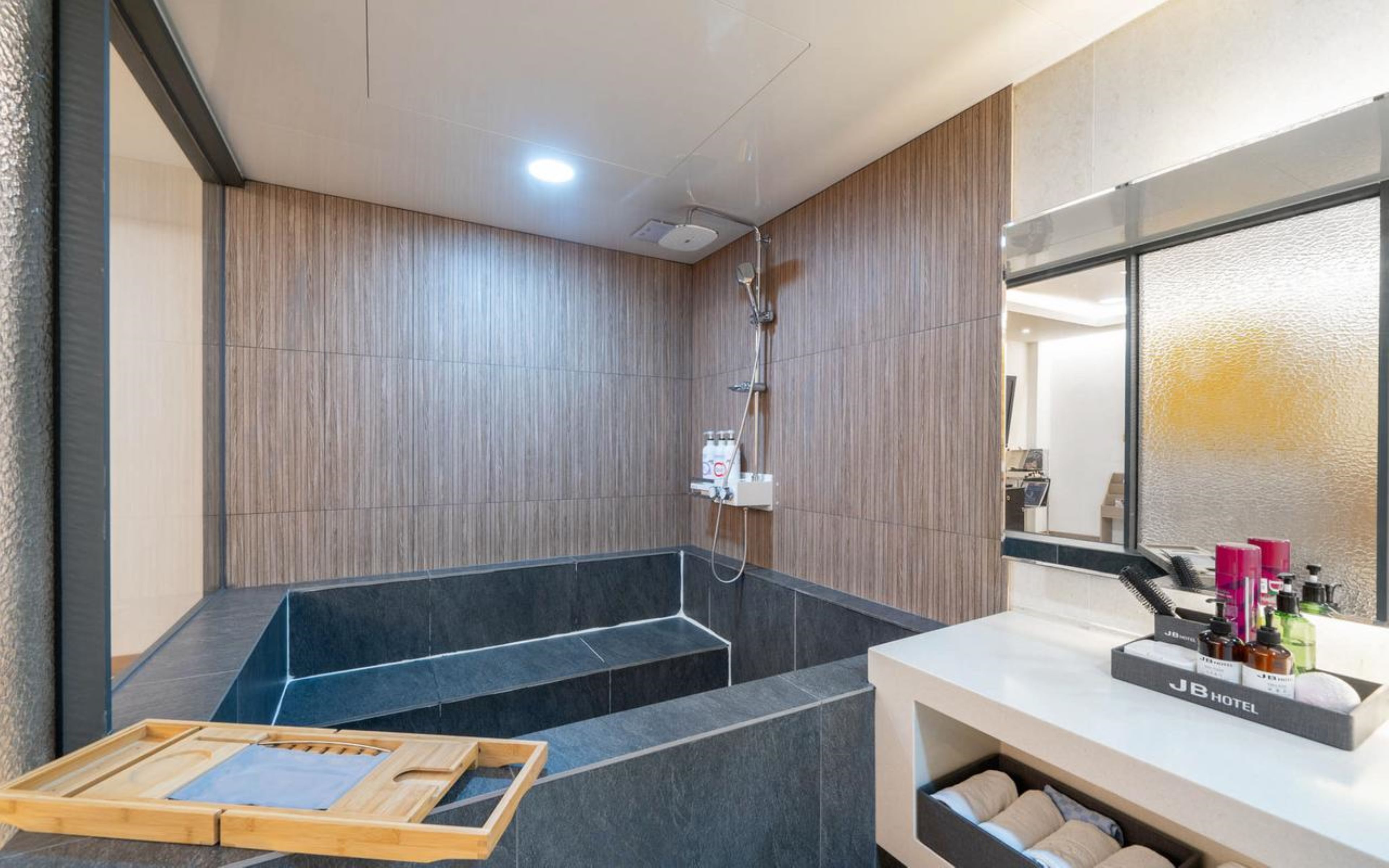 Un baño moderno con ducha, una bandeja de madera y un cartel de J.B. Hotel.