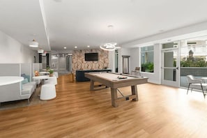 A modern indoor space with a pool table, seating area, and a large window providing a view of the outdoors. - Landing | Modern 1BD, Gym, Courtyard (Concord)