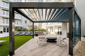 An outdoor patio area with a pergola, seating, and a view of the building's balconies. - Landing | Amazing 1BD, Courtyard, Gym (Concord)