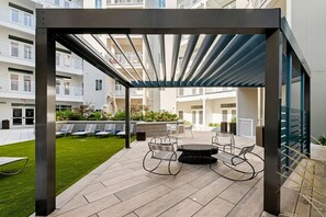 Ein Außenbereich mit Terrasse, einem Pergola, Sitzgelegenheiten und Blick auf die Balkone des Gebäudes.