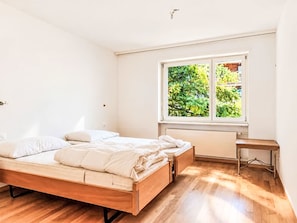 A bedroom with a wooden bed, a small desk, and a window with a view of greenery. - 3BR Finja by Interhome (St Niklaus)