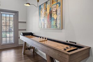 A room with a foosball table, a window with blinds, and a large abstract painting on the wall. - Landing | Beautiful 2BD, Clubhouse, Gym (Chattanooga)