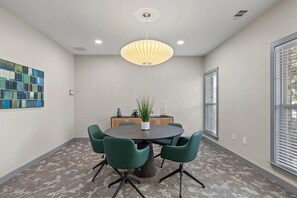 A conference room with a round table, green chairs, a potted plant, and a pendant light. - Landing | Modern 2BD, Clubhouse, Gym (Chattanooga)