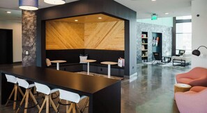A modern lounge area with a central wooden partition, seating, and a bar with stools. - Landing | Amazing 1BD, Clubhouse, Gym (Durham)